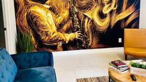 Una sala de estar con un cuadro abstracto grande, un sofá azul, una mesa de centro de madera y un sillón amarillo.