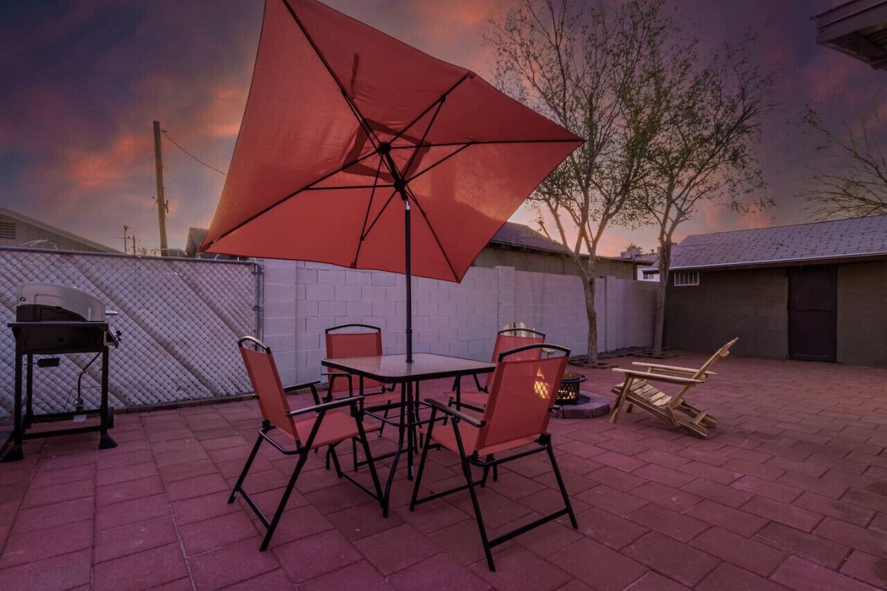 Une terrasse extérieure avec une table et des chaises, un barbecue et un grand parasol.