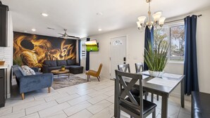 Una sala de estar moderna con un mural grande, un comedor con mesa y sillas, y un televisor montado en la pared.