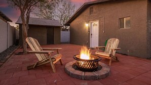 Un patio trasero con un brasero, dos sillas Adirondack y un patio de ladrillo.