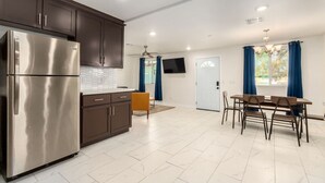 Una cocina moderna con armarios oscuros, un refrigerador de acero inoxidable, una zona de comedor con mesa y sillas, y un ventilador de techo.