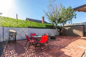 A patio with a table and chairs, a hammock, and a brick wall with a green hedge.