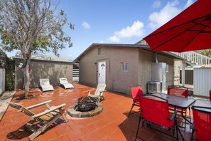 A patio with a fire pit, lounge chairs, and a red umbrella.