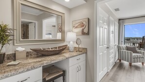 Une salle de bain avec un grand miroir, un lavabo sur colonne, un porte-serviettes et une plante en pot.