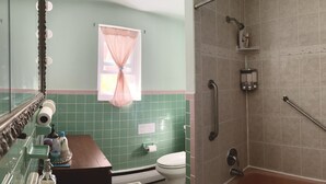 Une salle de bain avec un mur recouvert de carreaux verts, des toilettes blanches, un lavabo avec un miroir et un espace douche.