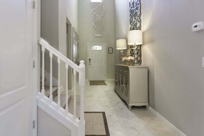 A hallway with a white staircase, a door, a cabinet with two lamps, and a decorative wall piece.