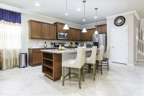 A kitchen with wooden cabinets, stainless steel appliances, a central island with bar stools, pendant lighting, and a clock on the wall.