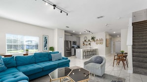 A modern living room with a blue sofa, a glass coffee table, and a kitchen in the background. - Roomy Family Home-Sleeps 16 | 109 (Kissimmee)