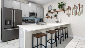 A modern kitchen with a central island, bar stools, stainless steel appliances, and decorative wall art. - Roomy Family Home-Sleeps 16 | 109 (Kissimmee)