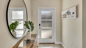 A hallway with a white door, a round mirror, a wooden bench, and a potted plant. - Stylish Family Home | Private Pool | 111 (Kissimmee)