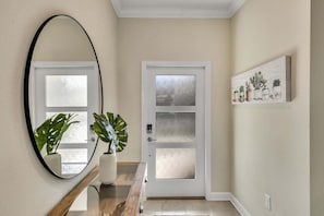 A hallway with a white door, a round mirror, and a potted plant.