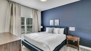 A bedroom with a bed, bedside tables, a window with curtains, and a wall with two framed pictures. - Stylish Family Home | Private Pool | 111 (Kissimmee)