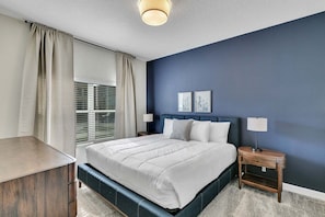A bedroom with a bed, bedside tables, a window with curtains, and a wall with two framed pictures.