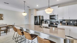 A modern kitchen with a central island, stainless steel appliances, and pendant lighting. - Stylish Family Home | Private Pool | 111 (Kissimmee)