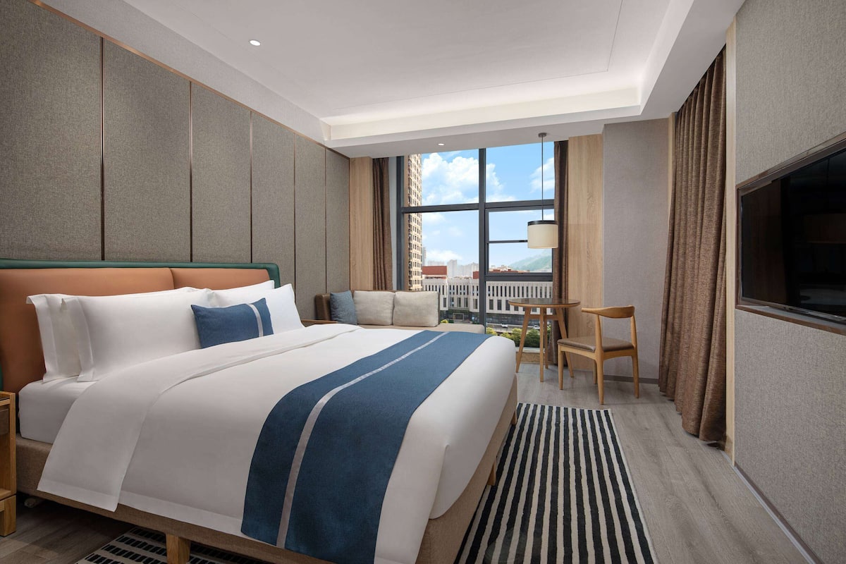 Quarto de hotel com uma cama grande, uma escrivaninha, uma cadeira e uma televisão.