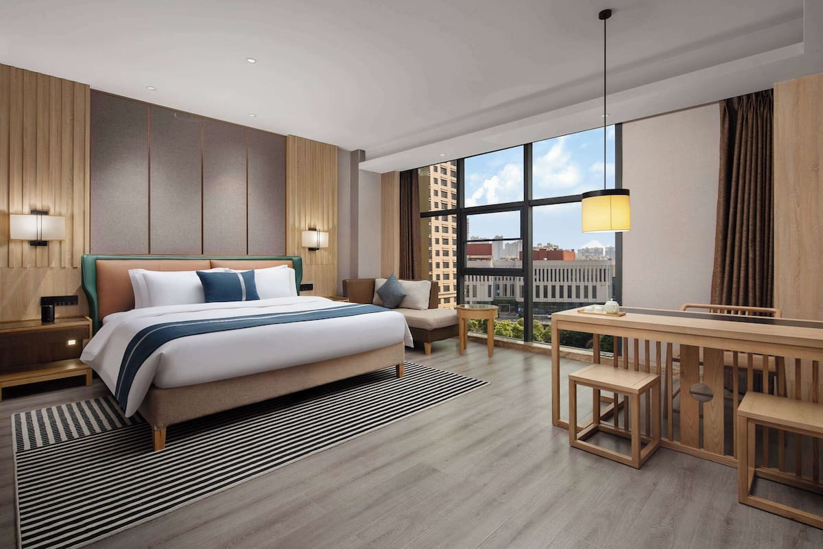 Quarto de hotel moderno com uma cama grande, uma escrivaninha e vista para a cidade.