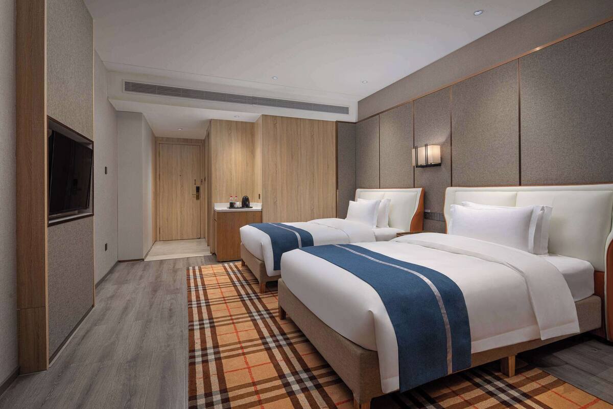 Quarto de hotel com duas camas, televisão, mesa de cabeceira e porta de banheiro.