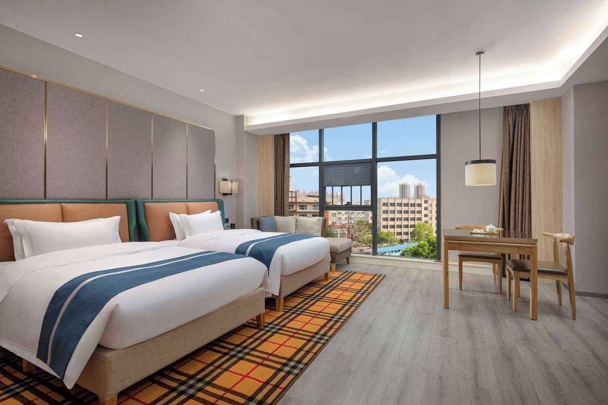 Quarto de hotel com duas camas, uma mesa de jantar e vista para a paisagem urbana.