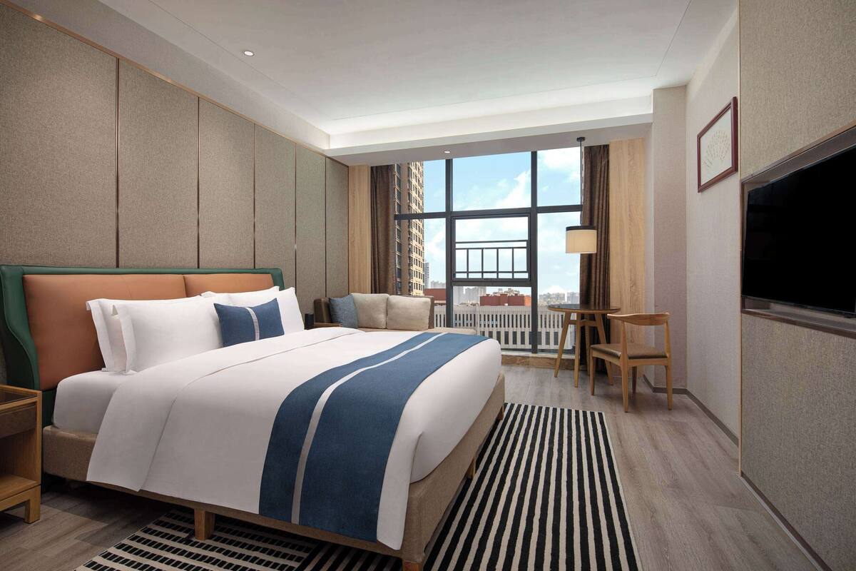 Quarto de hotel com uma cama grande, uma escrivaninha e uma televisão.