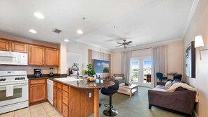 Une cuisine moderne avec un îlot central, un coin repas avec un canapé et des chaises, et un salon avec un divan et un téléviseur.