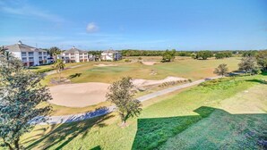 Un parcours de golf avec des bunkers de sable, un ciel dégagé et une rangée de bâtiments en arrière-plan.