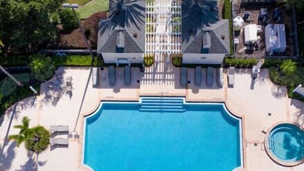 Une grande piscine rectangulaire, avec une plus petite piscine circulaire, le tout entouré de chaises longues et de palmiers.