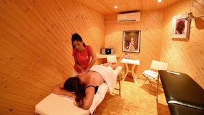 Une pièce en bois comprenant une table de massage, un massothérapeute et une petite table sur laquelle sont posées des bouteilles.