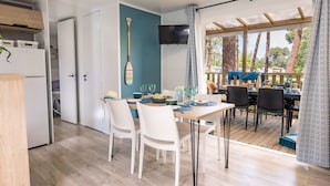 Un coin repas avec une table dressée pour quatre personnes, un téléviseur fixé au mur et une vue sur l’extérieur grâce à de grandes fenêtres.