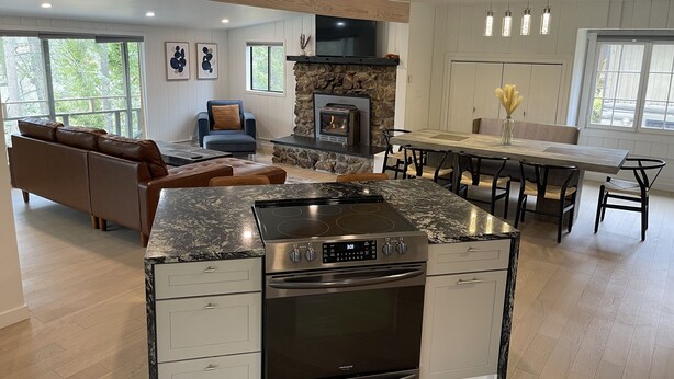 Una cocina moderna con una isla central, horno empotrado y una chimenea de piedra. Hay un comedor con una mesa y sillas de madera.