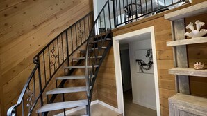 Una escalera de madera con barandal negro que lleva a un entresuelo con una puerta blanca y una repisa con adornos.