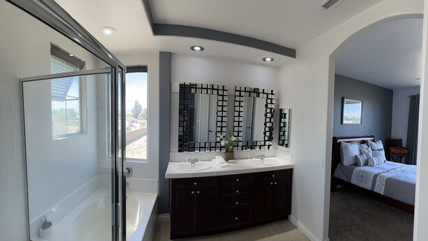 A modern bathroom with a glass shower enclosure, a double vanity with dark cabinets, and a large mirror with a geometric pattern.