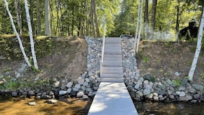 Un puente de madera sobre un arroyo, flanqueado por un muro de piedra a cada lado, rodeado de árboles.