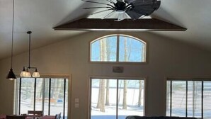 Amplia sala de estar con techo alto, ventilador de techo y gran ventanal con vistas a un paisaje nevado.