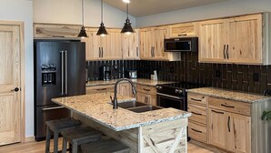 Una cocina moderna con armarios de madera, un refrigerador de acero inoxidable, horno empotrado y encimera de granito.