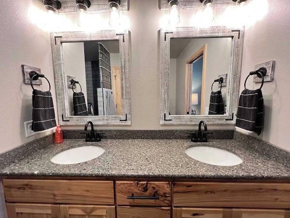 Une salle de bain avec deux lavabos, chacun étant surmonté d’un miroir. On trouve des meubles en bois sous les lavabos.
