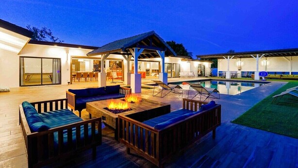 Un área junto a la piscina con mobiliario exterior, una fogata y un porche cubierto.