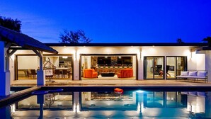 Una casa moderna con piscina, zona de estar exterior y barra.