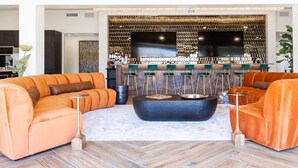 Una sala de estar moderna con dos sofás naranjas, una mesa de centro negra y una zona de bar con taburetes y un televisor.