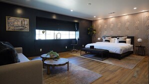Un dormitorio moderno con una cama grande, un escritorio y una silla. Hay una ventana con persianas y una planta en el escritorio.