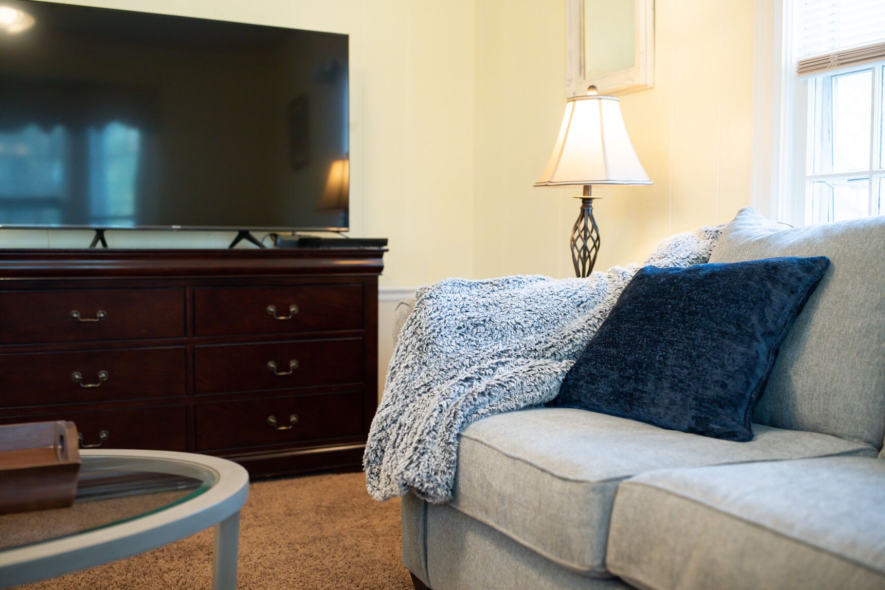 A living room with a sofa, a television on a stand, a lamp, and a glass table.