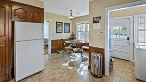 A kitchen with a refrigerator, wooden cabinets, a dining table with chairs, a trash can, and a calendar on the wall. - Home adjacent to Country Club, near Hospitals, Park, College and shopping. (Ada)