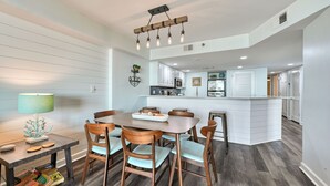 A dining area with a wooden table and chairs, a kitchen in the background, and a modern pendant light fixture. - Oceanfront Luxury Condo - 3BD with Gorgeous Views - Oceanfront Pool (North Myrtle Beach)