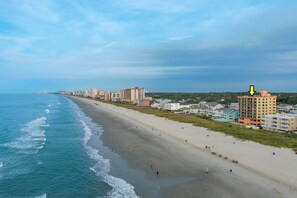 A coastal cityscape with a wide beach, buildings along the shore, and a clear sky.