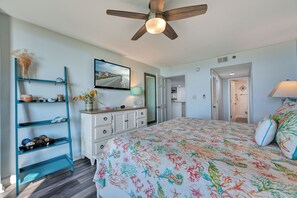 A bedroom with a bed, a ceiling fan, a TV, a bookshelf, and a door leading to another room.