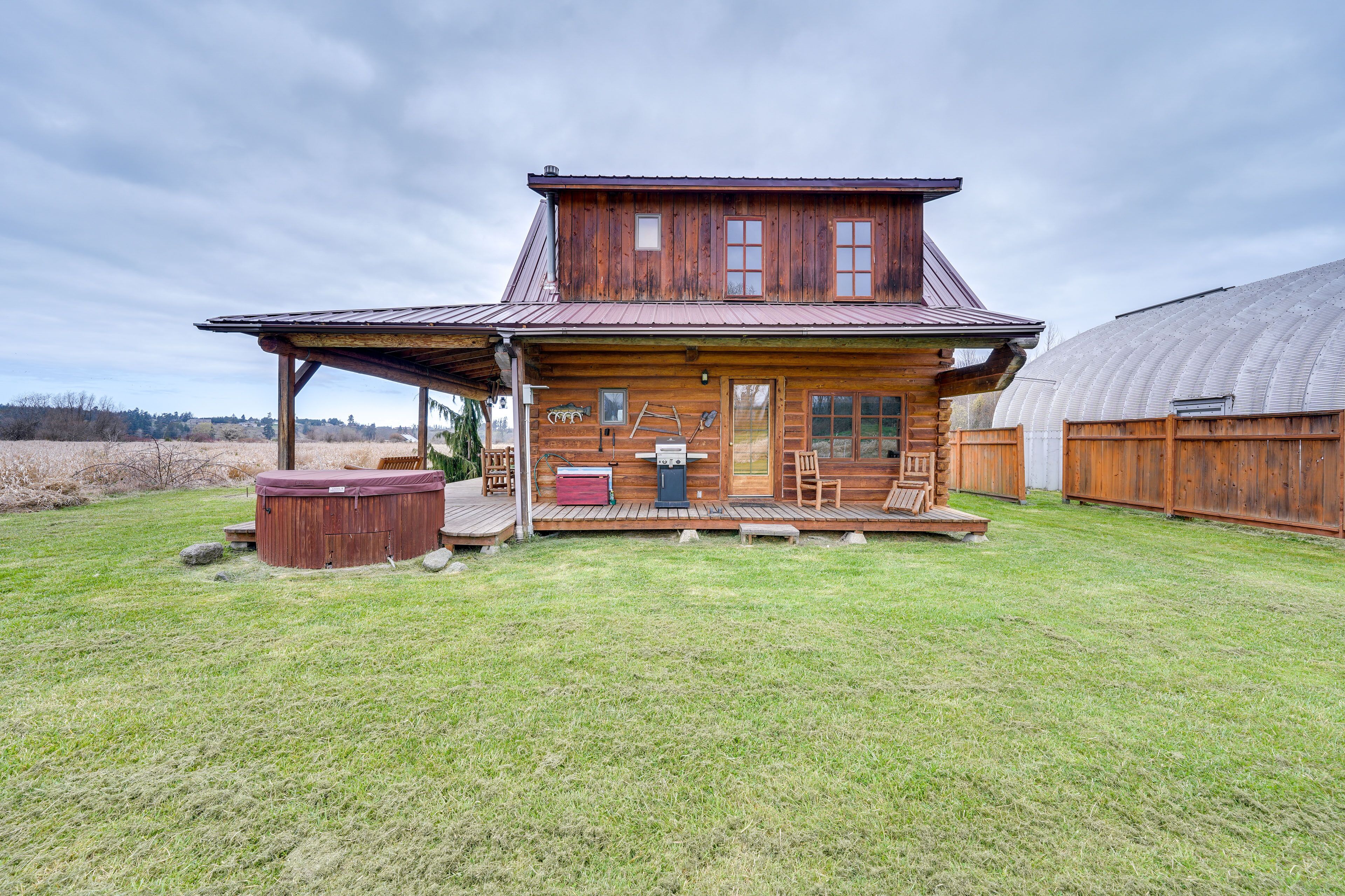 Une cabane en bois avec un porche, un jacuzzi et une grande grange en arrière-plan.
