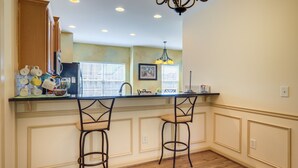 A kitchen with a central island, two bar stools, wooden cabinets, a chandelier, and a window with blinds. - Decatur Vacation Rental ~ 5 Mi to Downtown Decatur (Decatur)