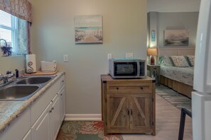 A compact kitchen with a microwave on a wooden cabinet, a sink, and a window with patterned curtains. - Sneads Ferry Vacation Rental Studio w/ Water Views (Sneads Ferry)