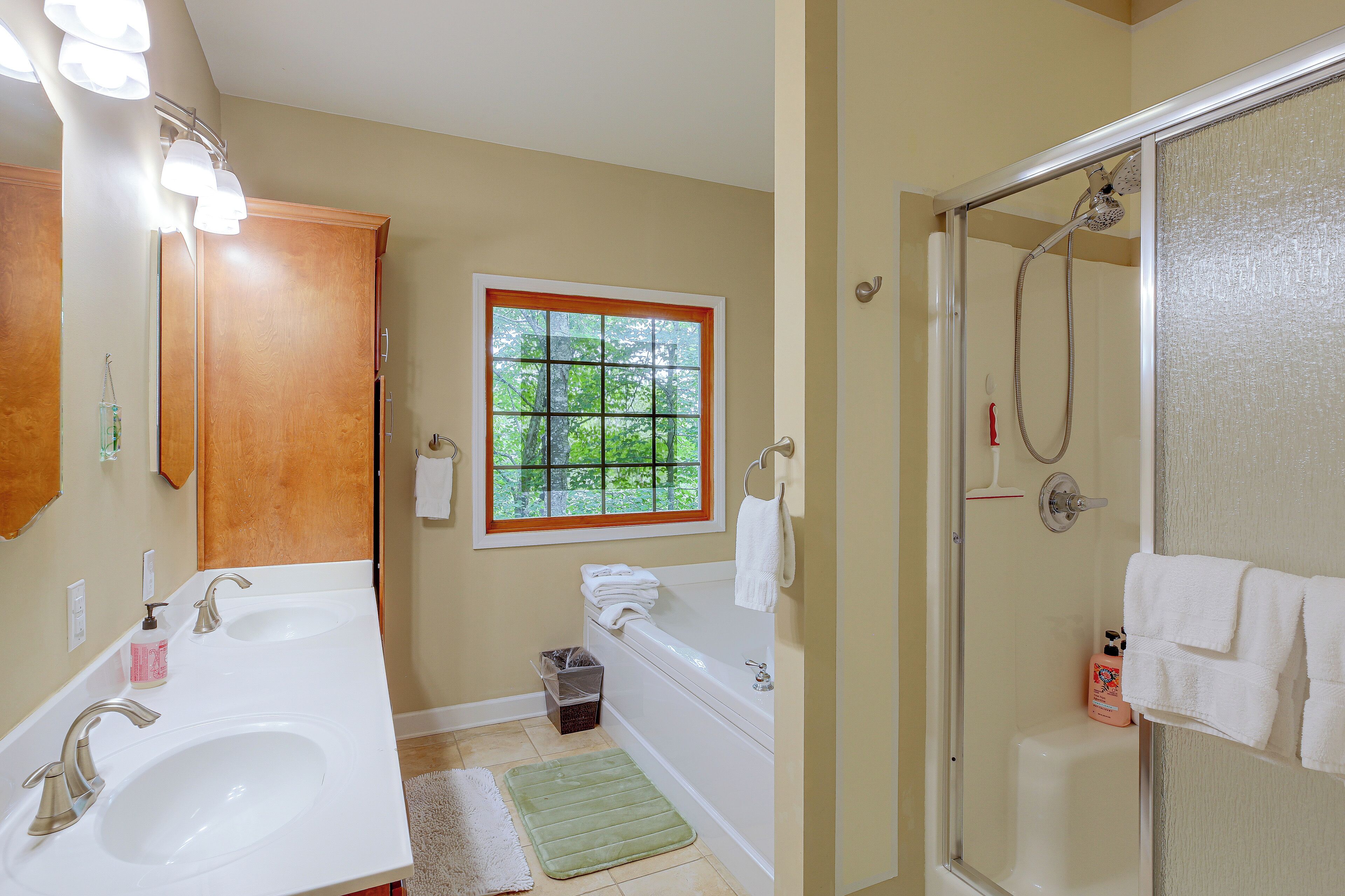 A bathroom with a double sink, a window, a shower, and a mirror.