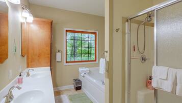A bathroom with a double sink, a window, a shower, and a mirror.