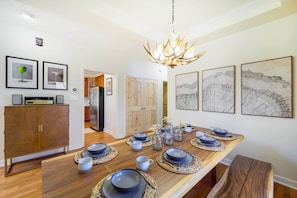 Een eetgedeelte met een houten tafel gedekt voor vier personen, omringd door omlijste kunstwerken, een moderne kroonluchter en een houten kast.